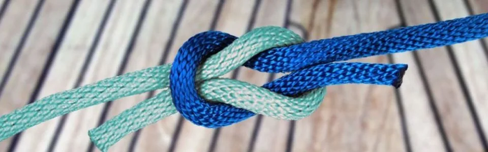 Kreuzknoten aus blauem und türkisem Tauwerk auf Schiffsplanken